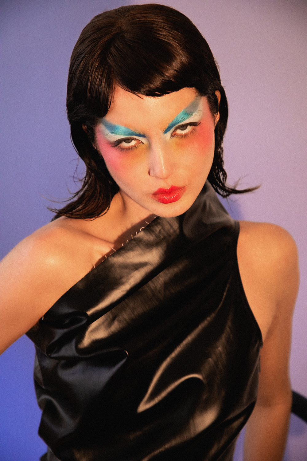 Close-up portrait of Autry with slicked dark hair and colorful makeup looking directly at the camera